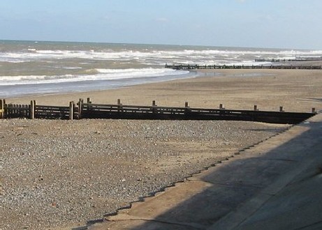 Photograph of a groyne stretching down a beach, with alot of coarse sediment this side of it, and much less, smaller, sediment on the other side